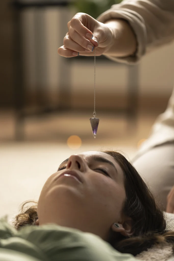 Femme allongée avec un pendule au dessus de sa tête tenu par la thérapeute